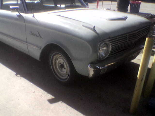 Light-colored car front with horizontal grille, round headlight, and chrome bumper