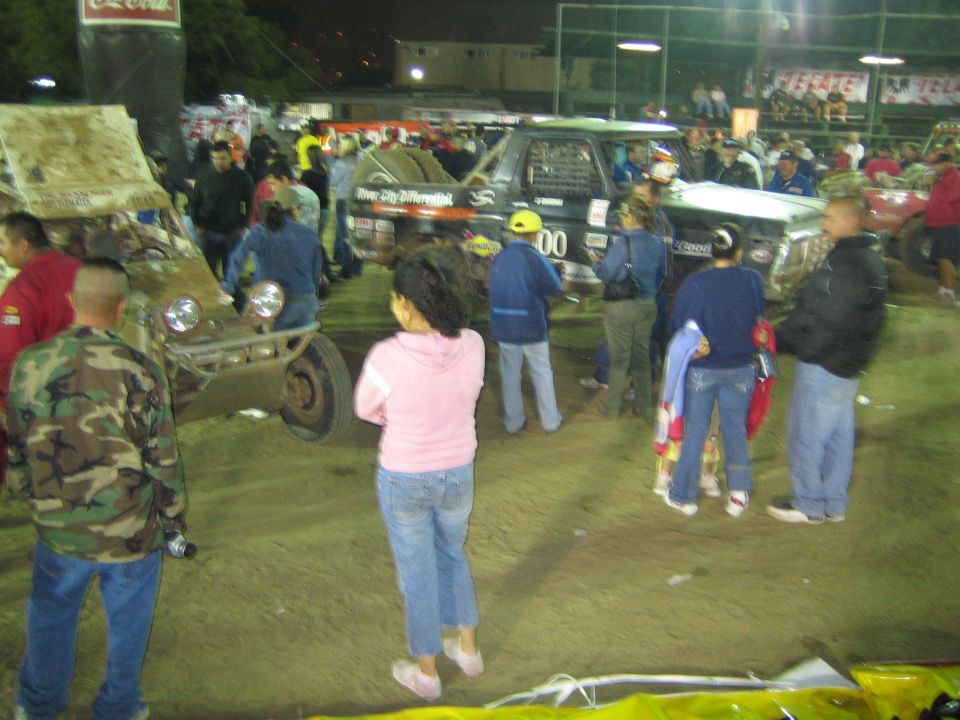 Crowd watching off-road race trucks in a floodlit dirt arena at night