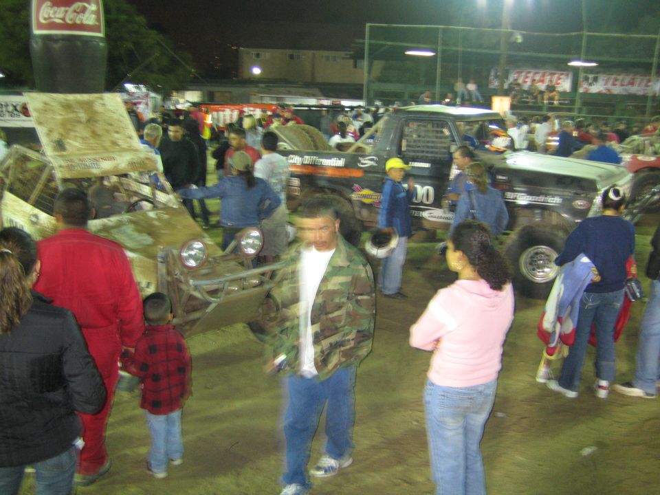 Busy crowd among off-road race vehicles in a dirt arena at night