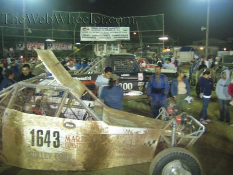 Gold-bodied off-road buggy number 1643 displayed in a dirt arena at night