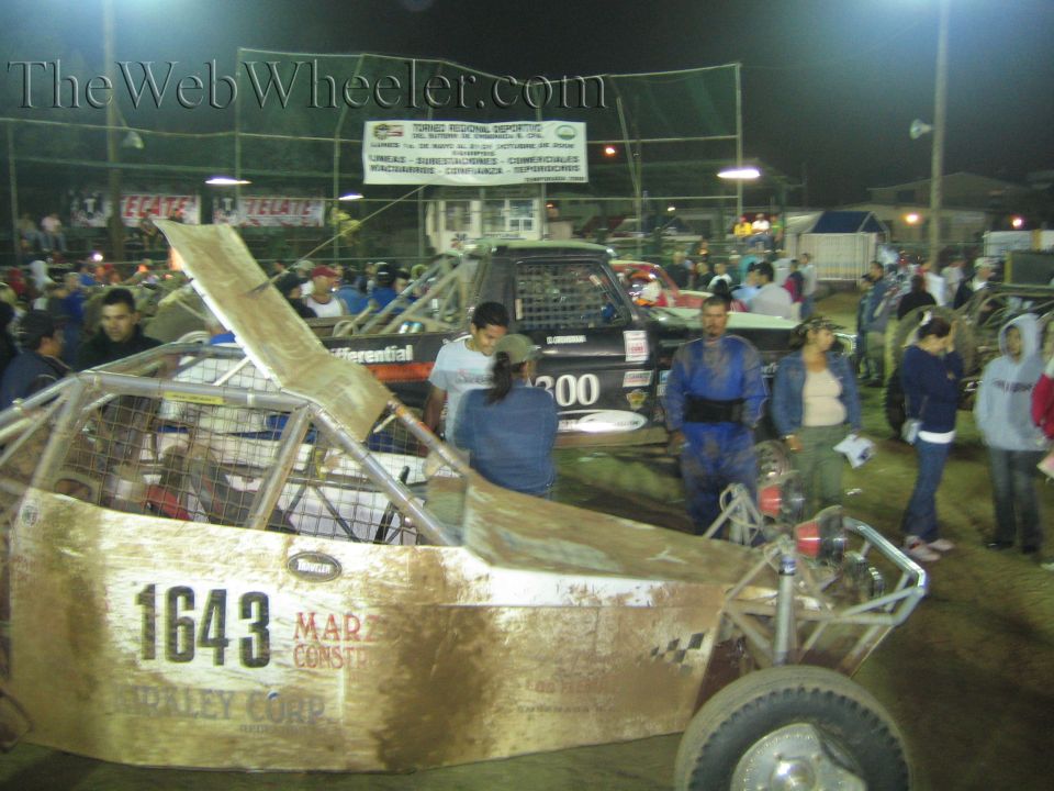 Gold-bodied off-road buggy number 1643 displayed in a dirt arena at night