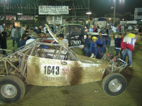 Gold off-road buggy 1643 and a black truck number 300 in a dirt arena at night