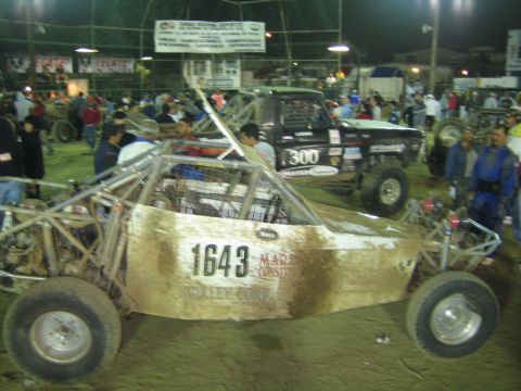 Gold off-road buggy 1643 beside black truck number 300 in a dirt arena at night