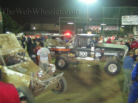 Black off-road race truck number 300 with twin spare tires in a dirt arena at night