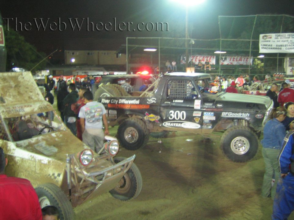 Black off-road race truck number 300 with twin spare tires in a dirt arena at night
