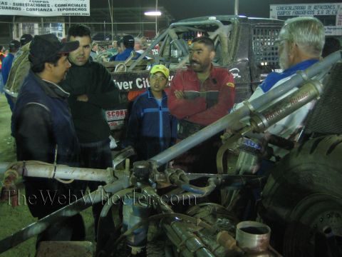 Men talking over a vehicle's exposed driveline and components at night