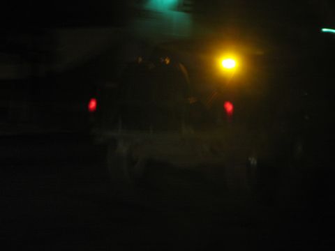 Dark blurred night photo of a vehicle with red taillights and a yellow light