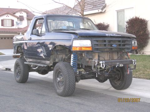 1994 Ford Bronco - This modified Ford Bronco is missing its front bumper and grille, revealing its lifted suspension and off-road modifications.