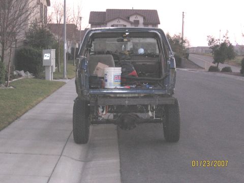 1994 Ford Bronco - Rear view of a modified blue Ford Bronco, showing its interior and aftermarket bumper, parked on a suburban street.
