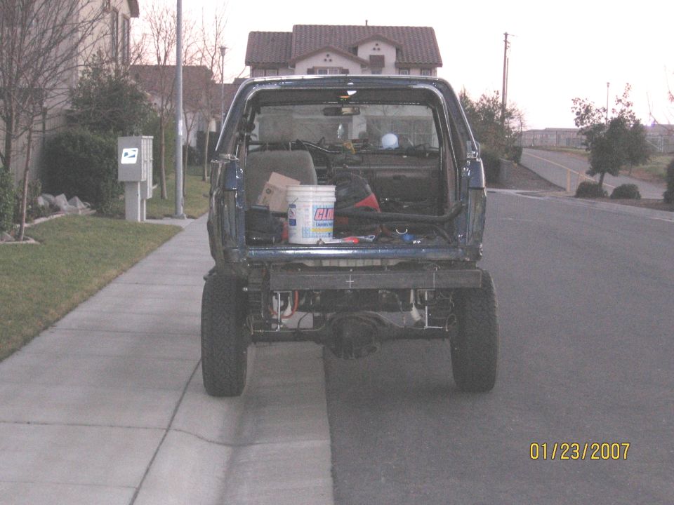 Rear of a lifted dark blue Ford Bronco with tailgate up and rear frame exposed, cargo inside