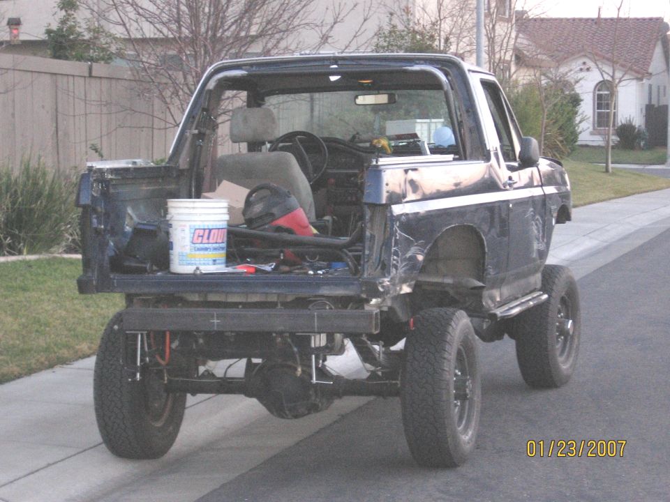 Dark blue Ford Bronco stripped rear, lifted on black wheels, parked on street