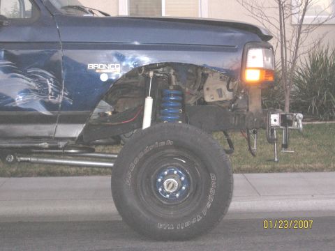 1994 Ford Bronco - A damaged blue Ford Bronco shows off its aftermarket suspension and missing front bumper.
