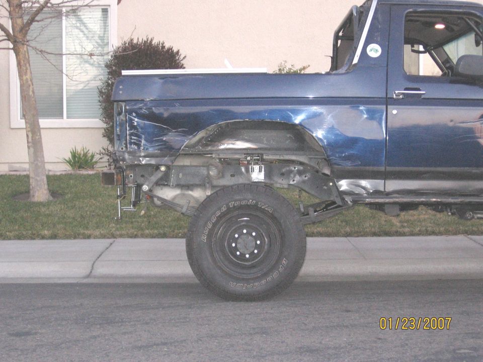 Dark blue Ford truck with rear fender removed, exposed frame and wheel, dented bedside