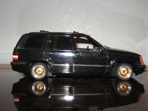 1977 Ford F-150 - A black SUV model with gold rims sits on a reflective surface, casting a mirror image.