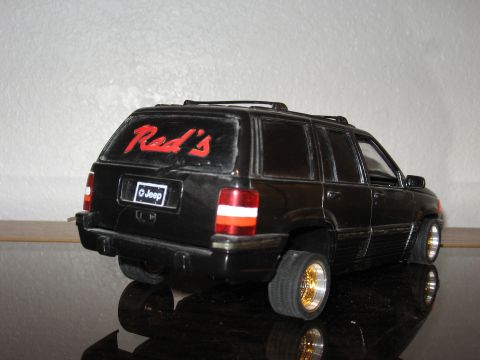 1977 Ford F-150 - A black Jeep Grand Cherokee model is viewed from the rear, displaying custom lettering and gold-accented wheels.