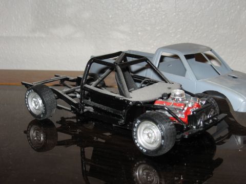 1977 Ford F-150 - A model truck chassis a roll cage and exposed engine is shown in the foreground, with a second model truck cab behind it.