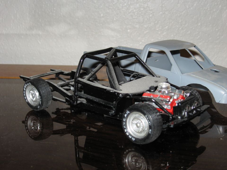 Model truck chassis with exposed engine and roll cage, with another model truck cab behind
