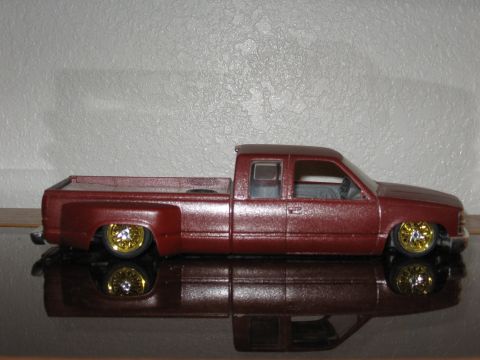 1977 Ford F-150 - A model pickup truck with a metallic maroon finish and gold wheels is displayed on a reflective surface.