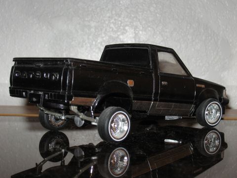 1977 Ford F-150 - A black Datsun pickup truck model is shown with its reflection on a shiny surface.