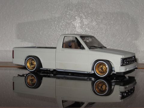 1977 Ford F-150 - A model pickup truck with custom gold wheels sits on a reflective surface against a textured background.