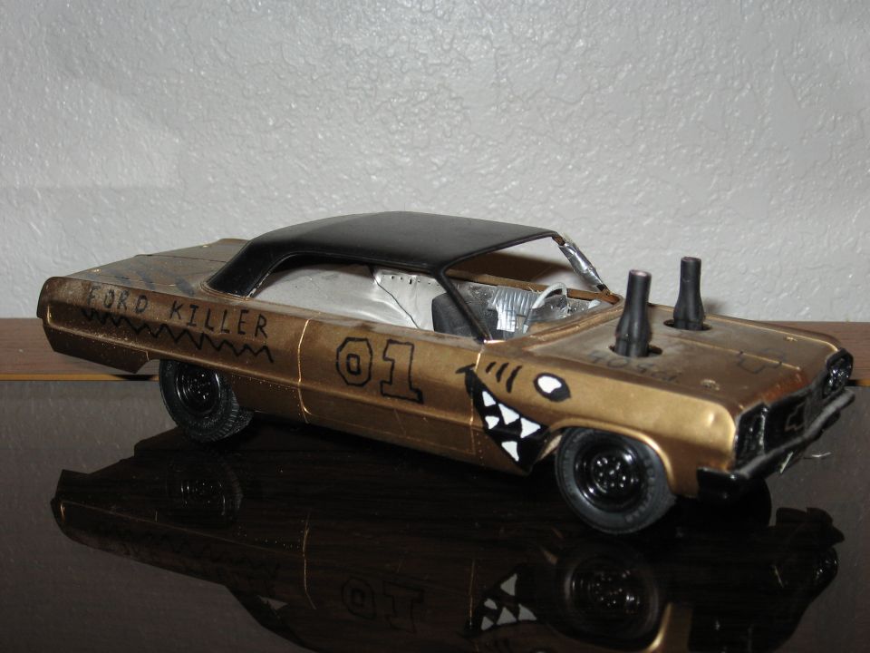 Gold model car with black roof, shark teeth on front fender, 'FORD KILLER' text, and twin exhaust pipes