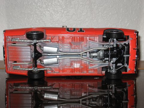 1977 Ford F-150 - The underside of a red model car, likely a replica, is viewed from below, revealing its mechanical details.