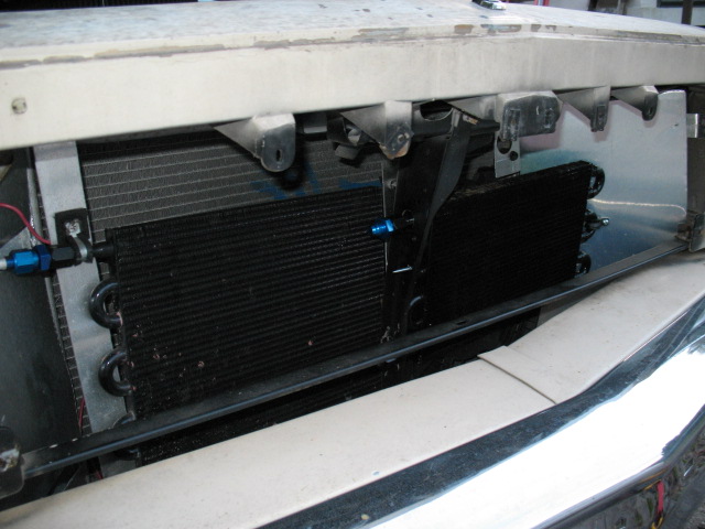 Close-up of a transmission cooler mounted in front of a radiator, with blue fittings