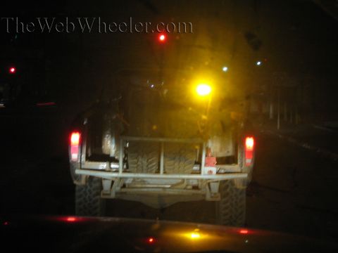 Rear view of a light-colored buggy with mud tires on a dark street at night