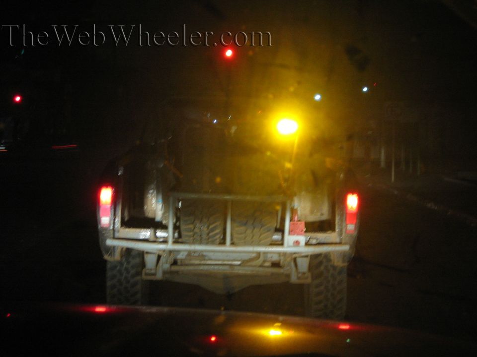 Rear view of a light-colored buggy with mud tires on a dark street at night