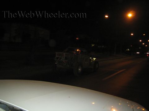Distant off-road buggy on a dark road at night seen over a white car hood