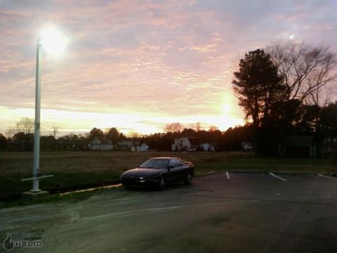 1993 Ford Probe - A black 1993 Ford Probe sits parked in a field as the sun sets, casting a warm glow across the sky.
