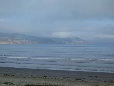 Overcast coastline with fog over hills and gentle surf along a sandy beach