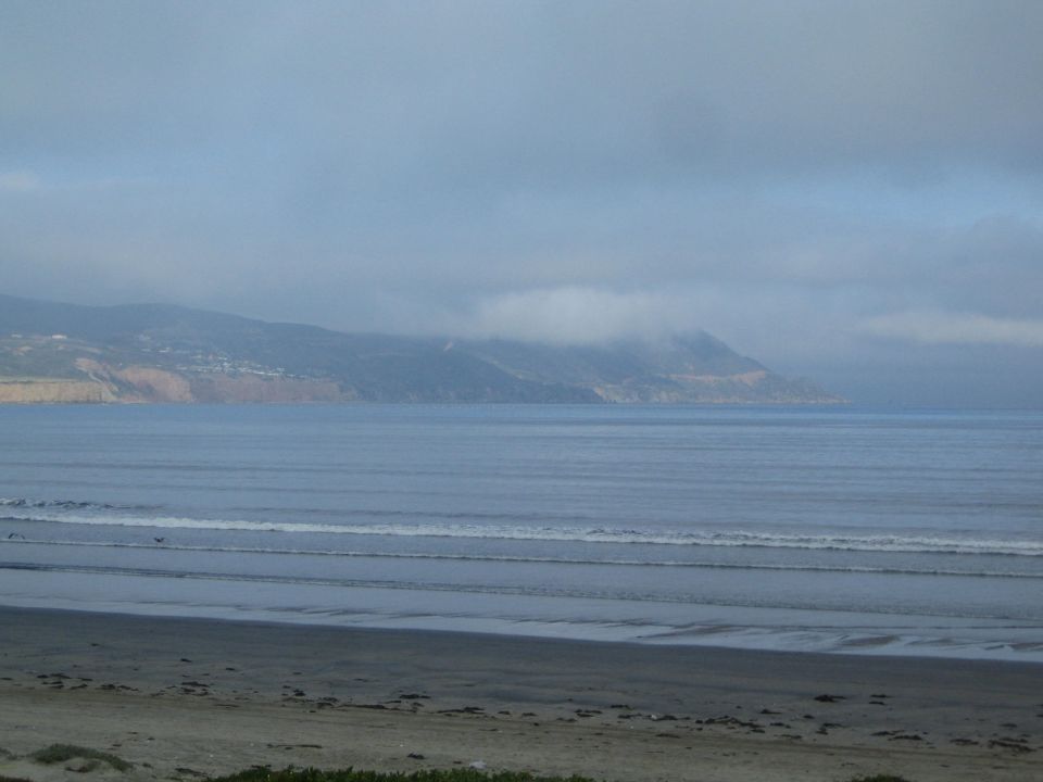 Overcast coastline with fog over hills and gentle surf along a sandy beach
