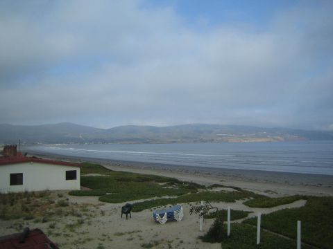 Beachfront house and lawn with chairs overlooking a wide bay under cloudy sky
