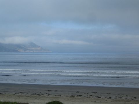 Overcast ocean view with rolling surf, sandy beach and fog-covered headland