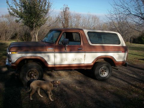 1978 Ford Bronco - A two-tone brown and white 1978 Ford Bronco is seen from the side, parked outdoors on a dirt path.