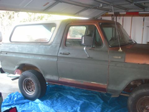 1978 Ford Bronco - A 1978 Ford Bronco is parked inside a garage, showing its side profile with primer gray and copper paint.