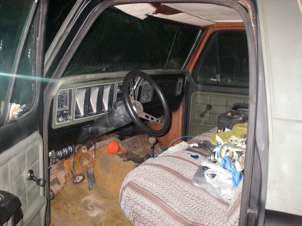 Vintage Ford truck cab interior with bare rusty floor, dash and blanket-covered bench seat