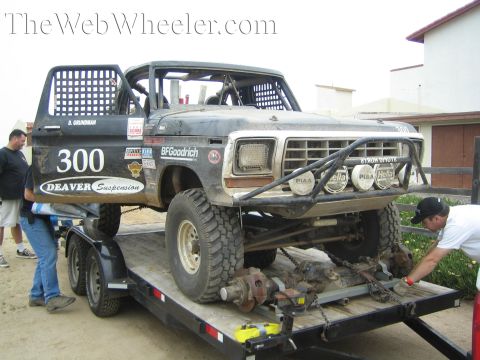 Black off-road race truck number 300 on a trailer with axles removed, men nearby