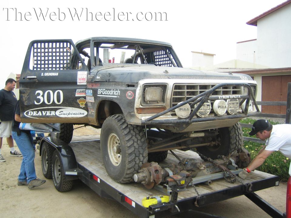 Black off-road race truck number 300 on a trailer with axles removed, men nearby