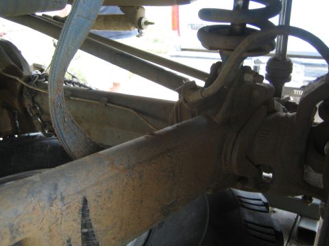 Dirty undercarriage view of an off-road vehicle's axle, coil spring and tie rod