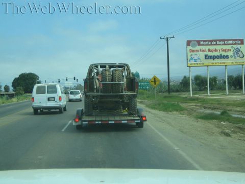 Off-road truck on trailer towed down a highway past a Spanish billboard
