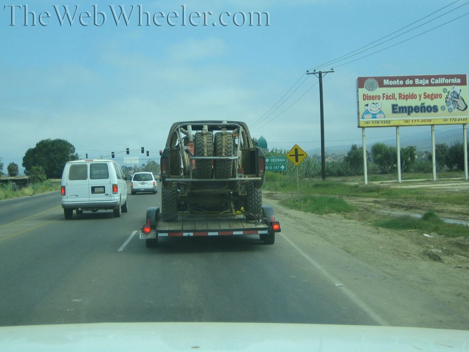 Off-road truck on trailer towed down a highway past a Spanish billboard