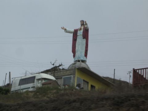Roadside statue of Jesus with outstretched arms atop a small building on a hill