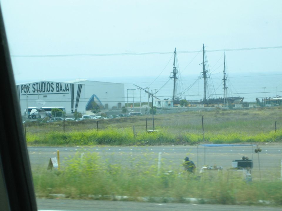 Tall ship masts behind a Fox Studios Baja building seen across a field