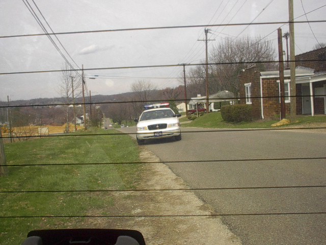 White police sedan with light bar approaching on a residential street, seen through a car window