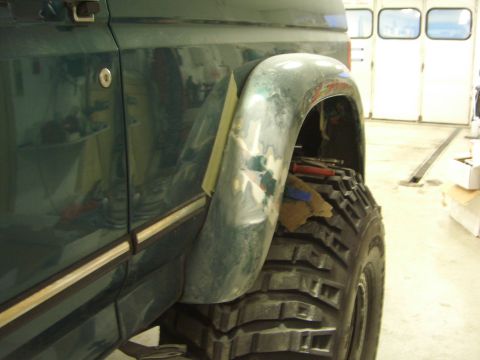 1996 Ford Bronco - Side view of a green 1996 Ford Bronco undergoing fender repair, with a large off-road tire visible.