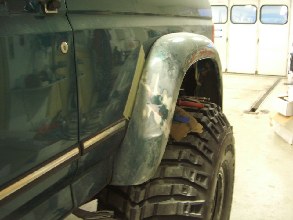 Green SUV front fender with primer flare over large mud tire during body work