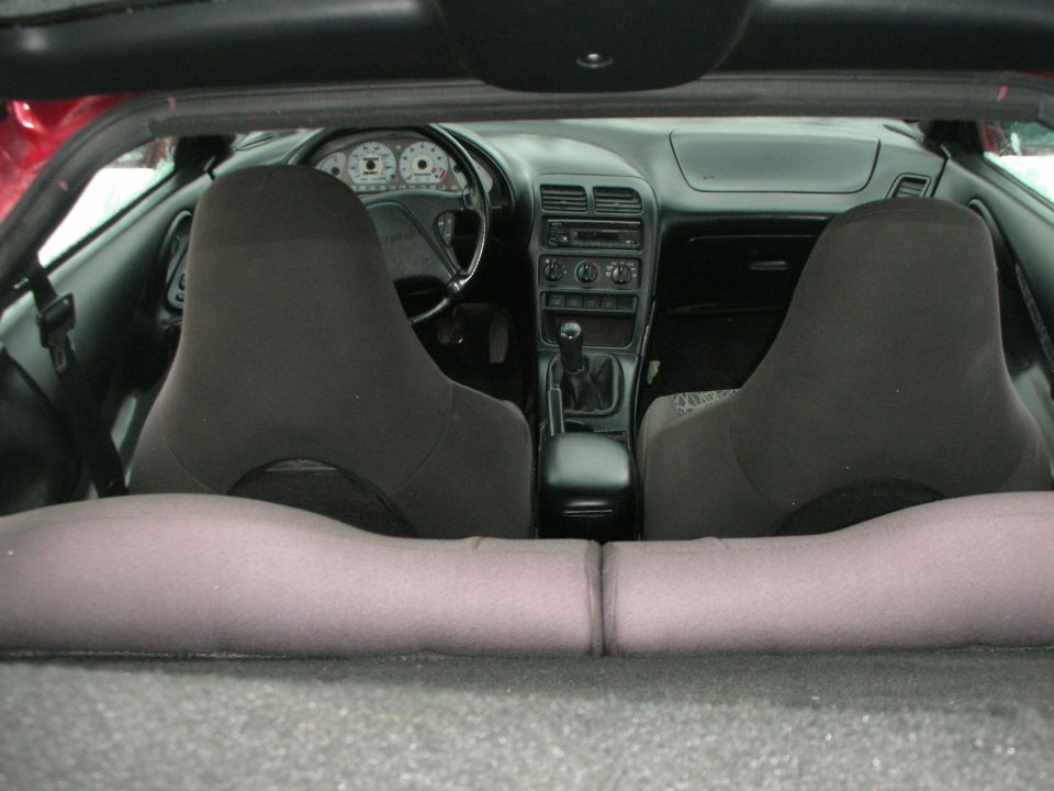View from rear hatch into coupe interior with two black seats and manual shifter