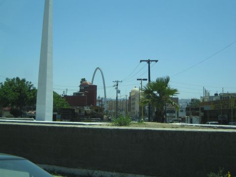 Arched monument and palm tree over a city street seen past a low concrete wall